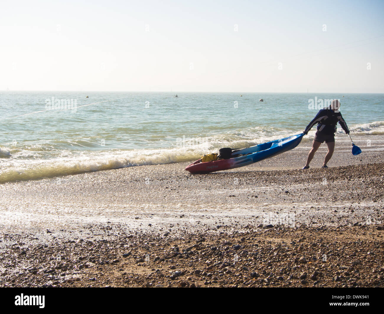 ein Mann zieht ein Meer Kajak aus dem Wasser und an einem Strand Stockfoto