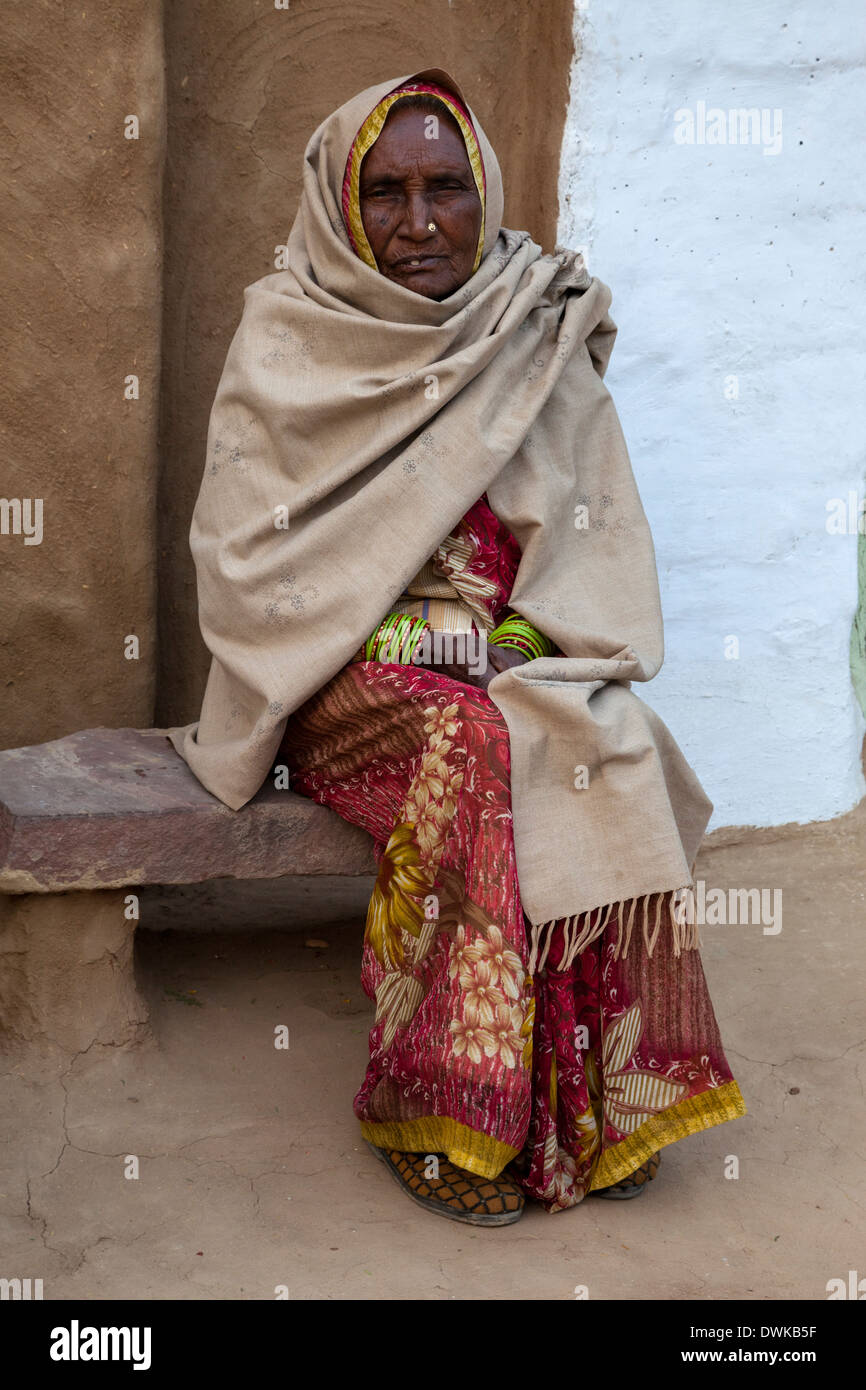 Bharatpur, Rajasthan, Indien. Alte Frau auf Stein Bank vor ihrer Tür. Sie trägt eine Dupatta (Schal) über ihren Kopf und Ihre Schultern. Stockfoto
