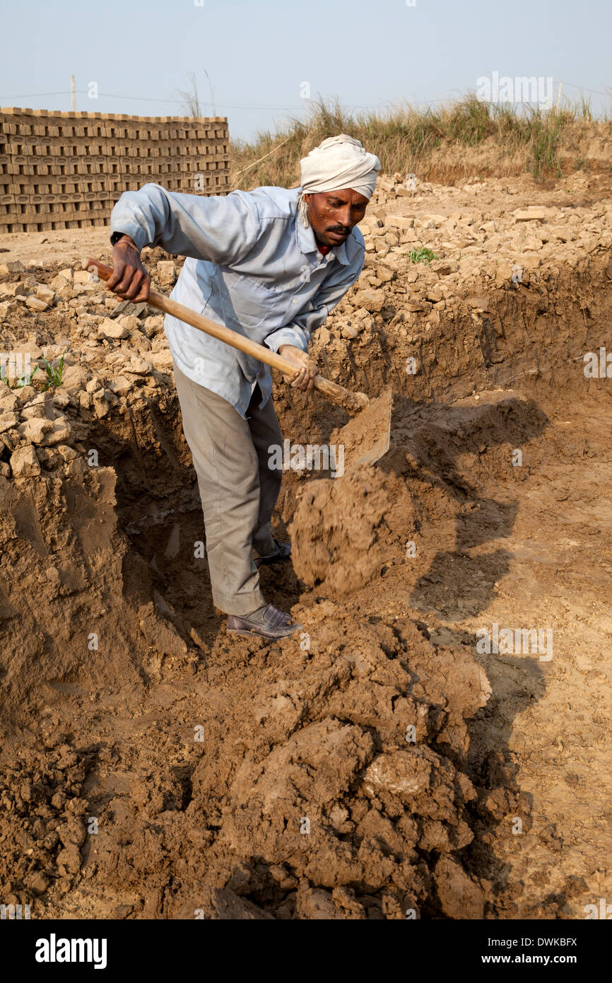 Rajasthan, Indien. Arbeiter lockert Erde in Schlamm für Ziegel Formen umgewandelt werden. Stockfoto