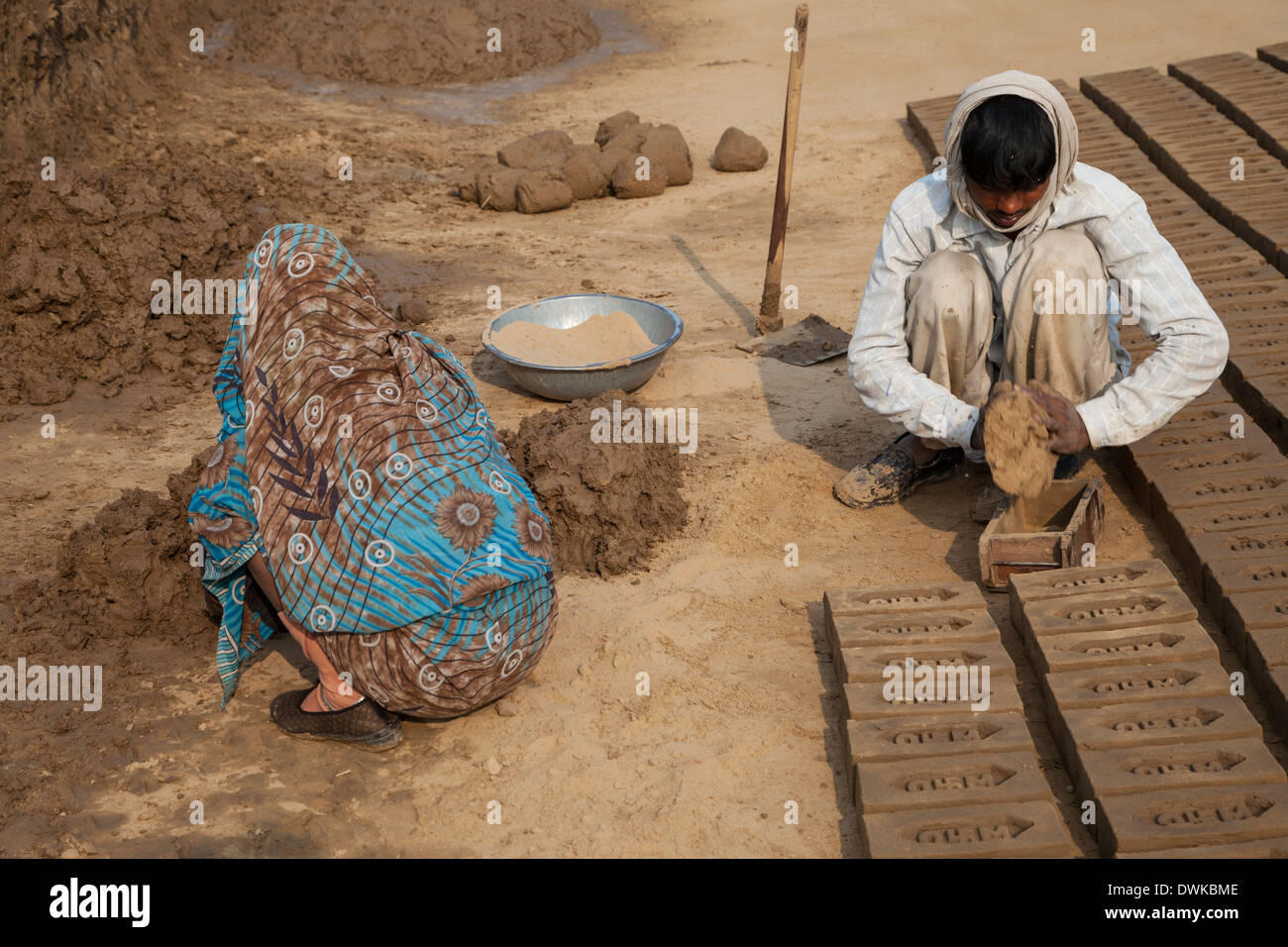 Rajasthan, Indien. Frau bereitet weichen Schlamm während Mann es in Backstein Form ausdrückt. Stockfoto