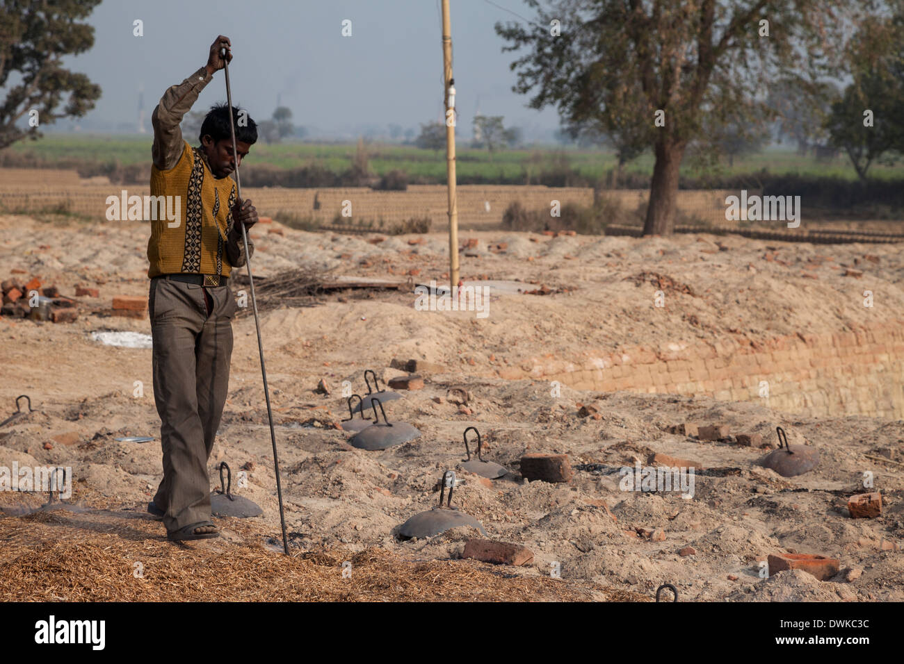 Rajasthan, Indien. Arbeitnehmer mit langer Rute, Holzspäne in den unterirdischen gemauerten Ofen zu rühren. Stockfoto
