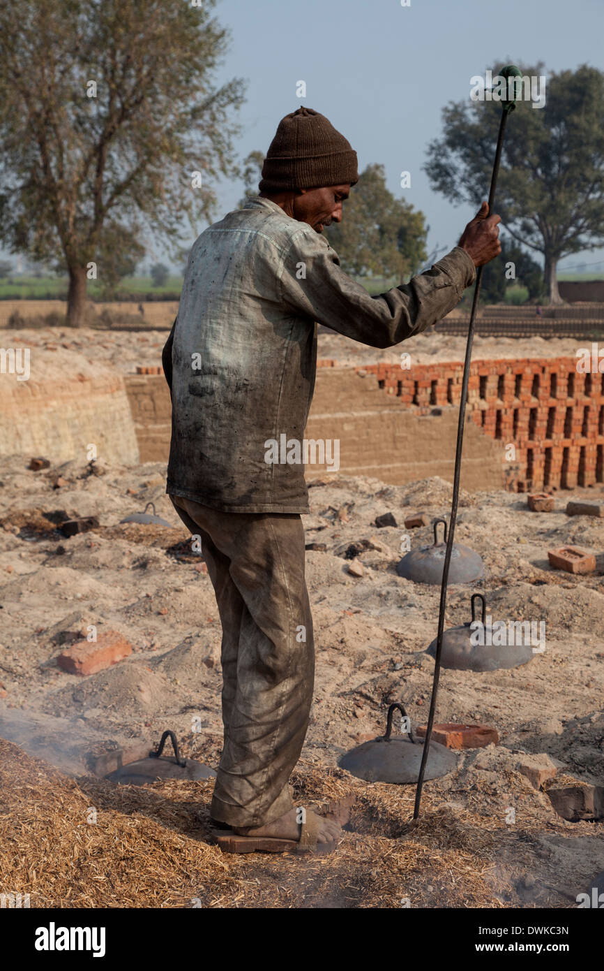 Rajasthan, Indien. Arbeitnehmer mit langer Rute, Holzspäne in den unterirdischen gemauerten Ofen zu rühren. Stockfoto