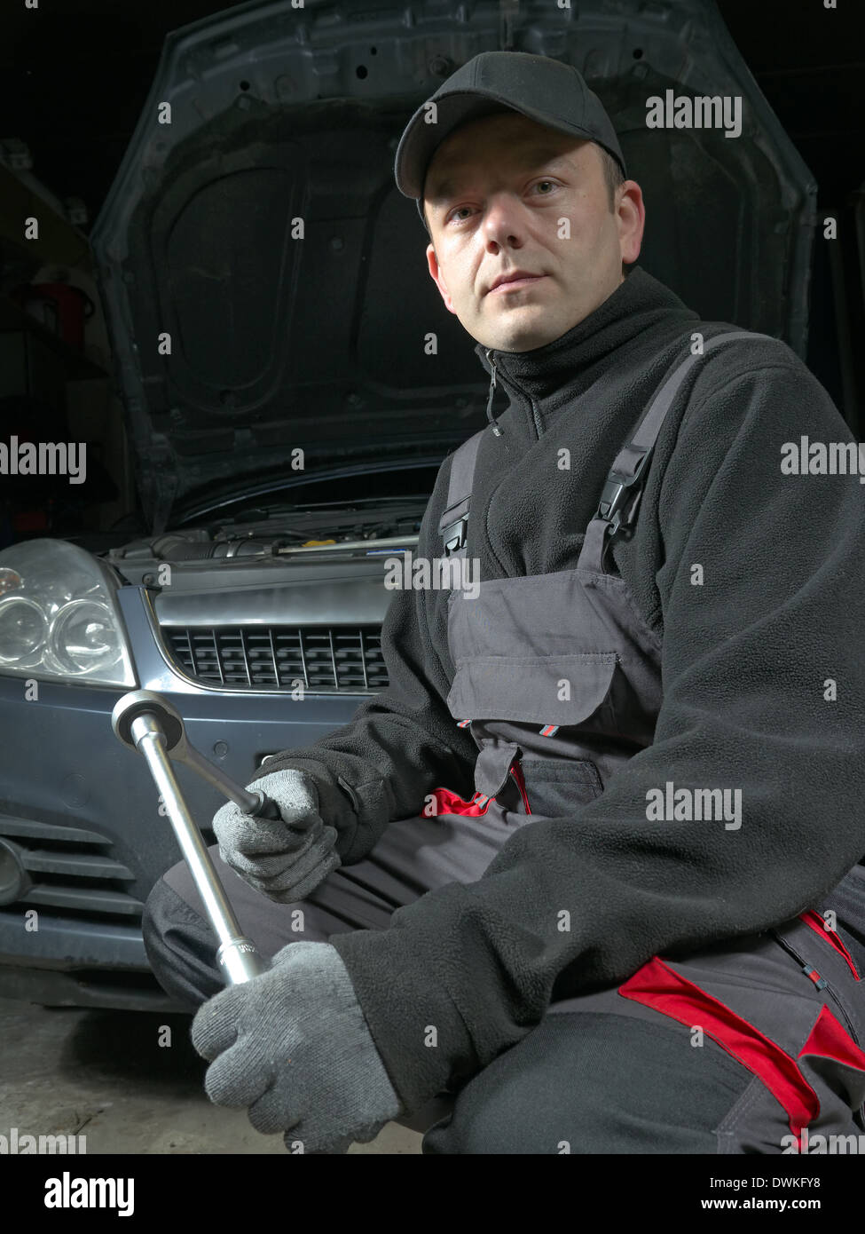 Kfz-Mechaniker posiert mit Steckschlüssel vor ein Auto mit angehobenen Haube Stockfoto