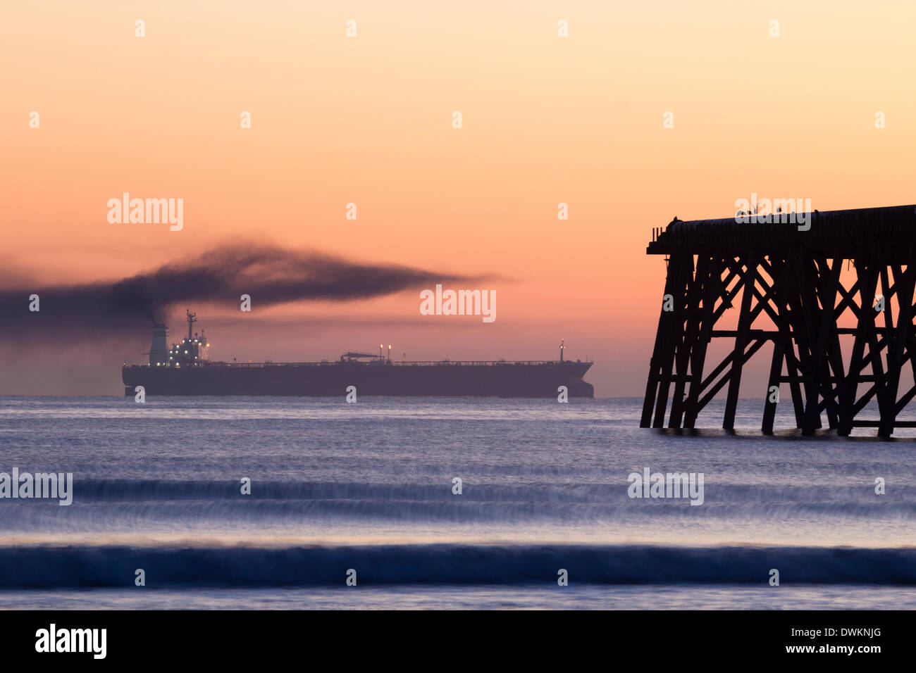 Schwarzer Rauch aus dem Öltankertrichter bei Sonnenaufgang, der am Steetley Pier in Hartlepool im Nordosten Englands vorbeiführt. UK Stockfoto