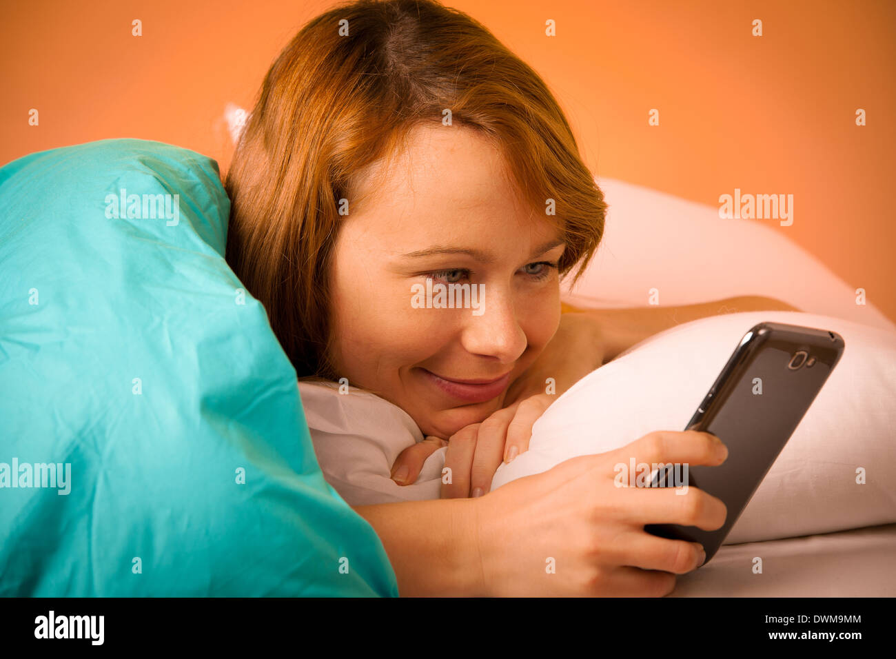 Hübsche Frau liest eine Sms auf Handy im Bett am Morgen Stockfoto