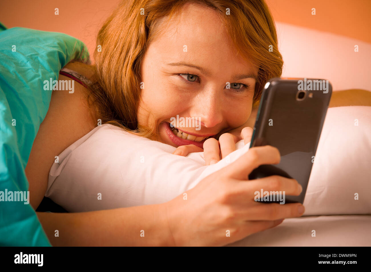 Hübsche Frau liest eine Sms auf Handy im Bett am Morgen Stockfoto