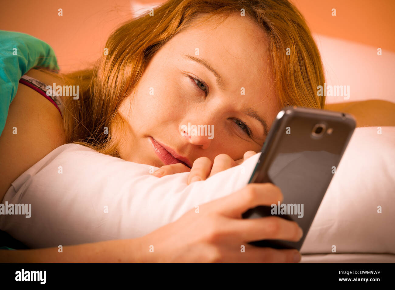 Hübsche Frau liest eine Sms auf Handy im Bett am Morgen Stockfoto
