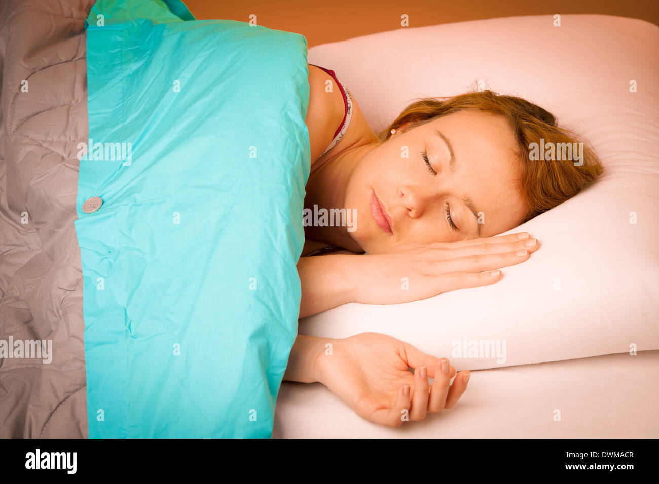 Frau liegend auf Kissen im Bett, bedeckt mit blauen Decke Stockfoto
