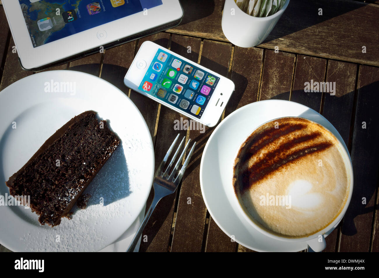iPhone 4 s, iPad 2 und Kuchen und Cappuccino auf Tisch im Sonnenlicht Stockfoto