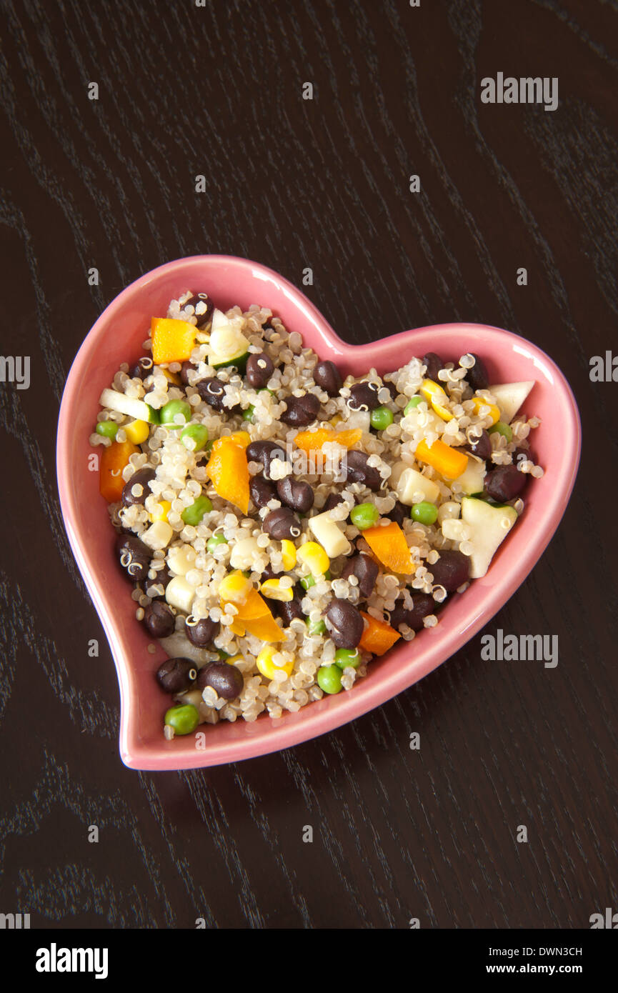 Herzförmige Schüssel mit Quinoa Salat auf einem dunklen Holztisch Stockfoto