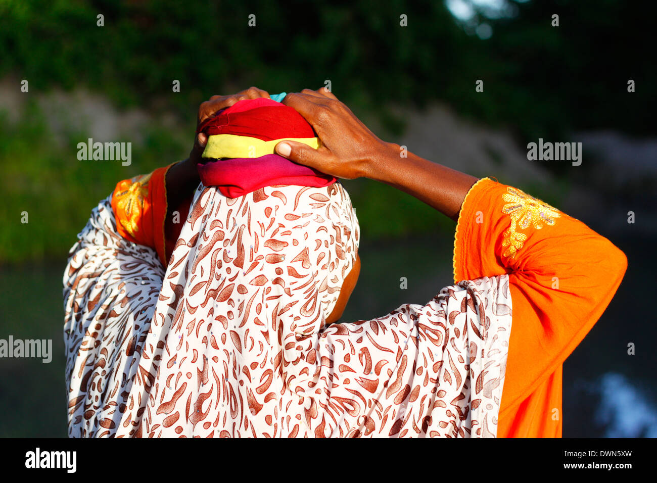 Frau legen Sie ein Tuch auf dem Kopf, einen vollen Eimer Wasser wieder zu Hause in Quirimbas National Park, Mosambik tragen zu können Stockfoto