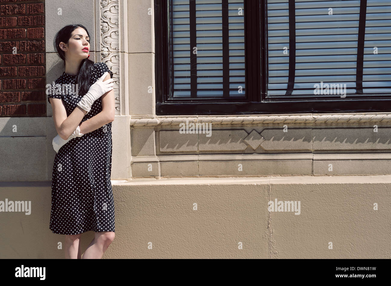 Ein weibliches Modell schlanke gegen eine Wand trägt eine Vintage inspiriert Polka Dot Kleid und weißer Handschuh wegschauen Stockfoto