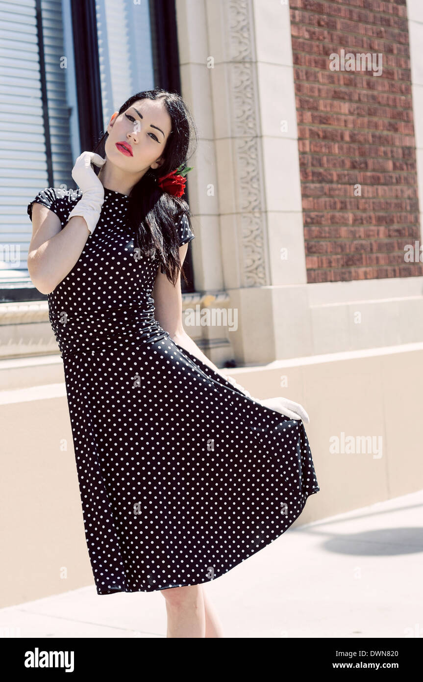 Ein weibliches Model posiert, inspirierte trägt eine Vintage Polka Dot Kleid und weißer Handschuh hält ihren Rock hoch Stockfoto