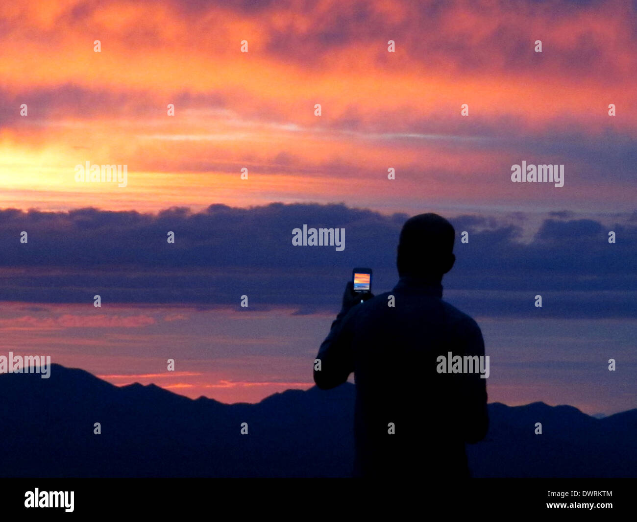 Ein Mann nimmt auf seinem Handy ein Foto von einem Sonnenuntergang. Stockfoto