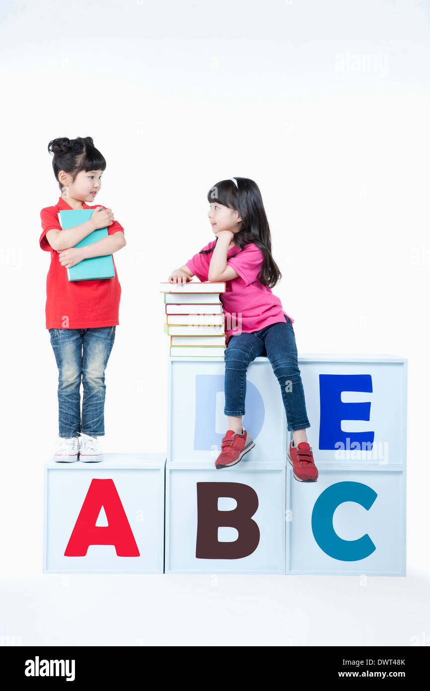 Kinder stehen und sitzen auf Alphabet Blöcke mit Büchern Stockfoto