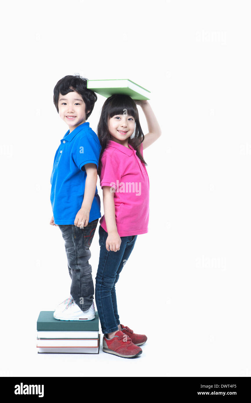 ein Junge steht auf Stapel Bücher, die Messung der Höhe mit einem Mädchen Stockfoto