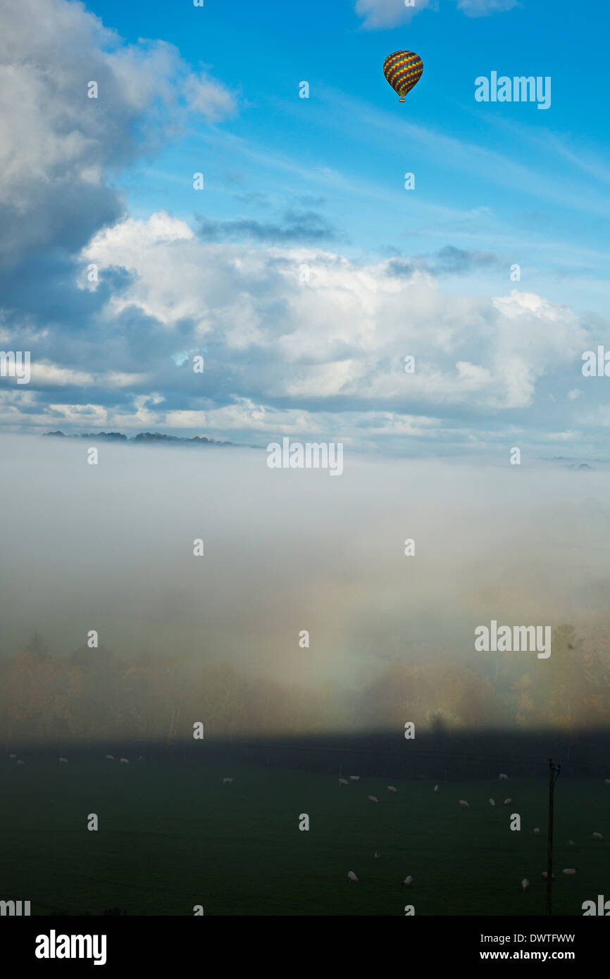 Ein Heißluftballon erhebt sich über den Wolken an einem nebligen Morgen Stockfoto