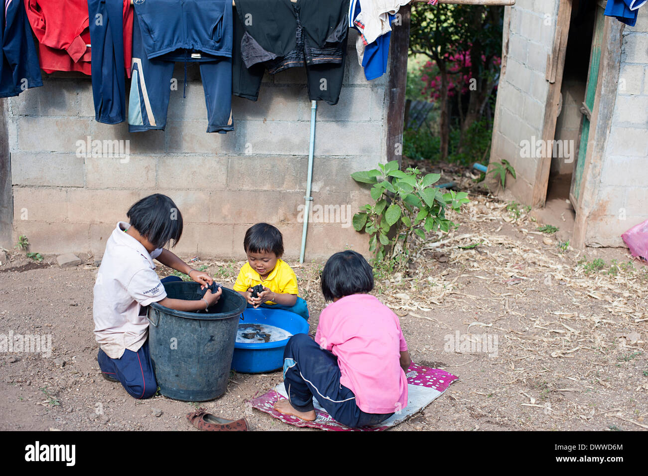 Drei Kinder Wäsche draußen in einem großen Eimer in Huay Pakoot Dorf im Norden Thailands. Stockfoto