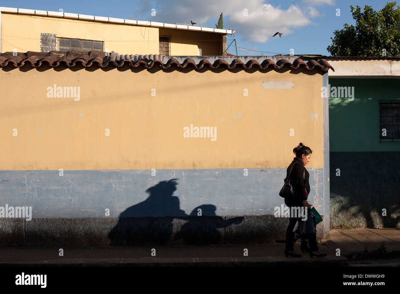 eine Frau geht vorbei an einer Wand als ihr von der Nachmittagssonne in Juayua auf die Rutas Schatten De La Flores in El Salvador Stockfoto