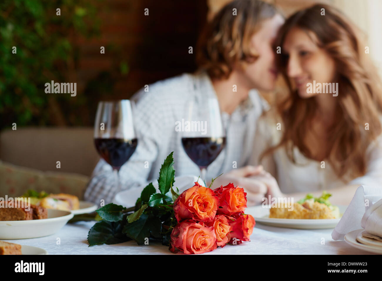 Ein paar rote Rosen am Tisch serviert und junge Liebhaber auf Hintergrund Stockfoto