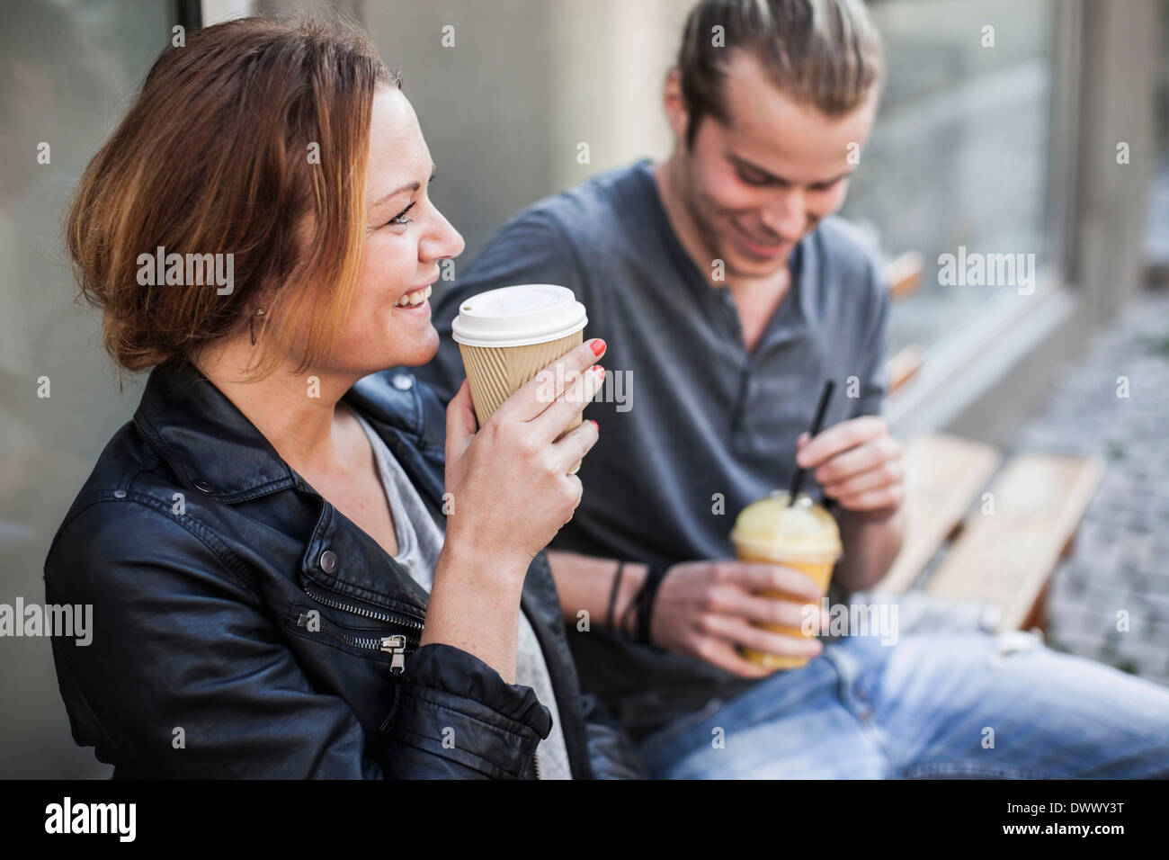 Glückliche Frau Kaffeetrinken in Einweg-Becher mit Mann auf Bank am Bürgersteig Stockfoto