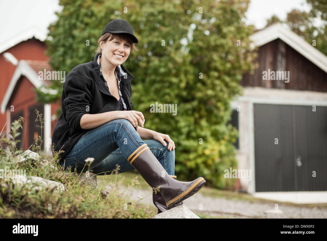 In voller Länge Portrait von zuversichtlich Bäuerin sitzt auf Felsen auf der farm Stockfoto