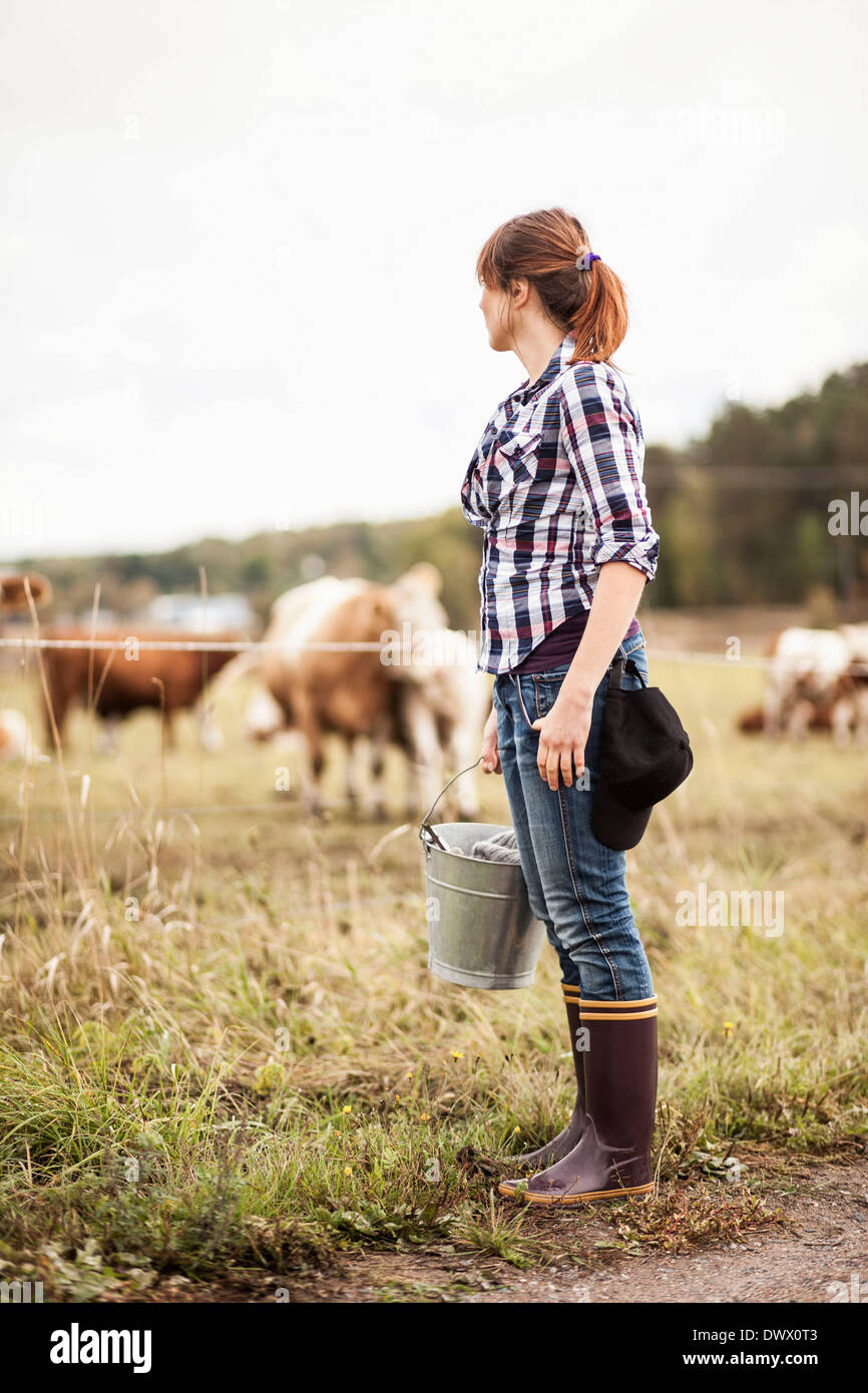 Bäuerin mit Eimer stehen auf Feld mit Tiere grasen im Hintergrund Stockfoto