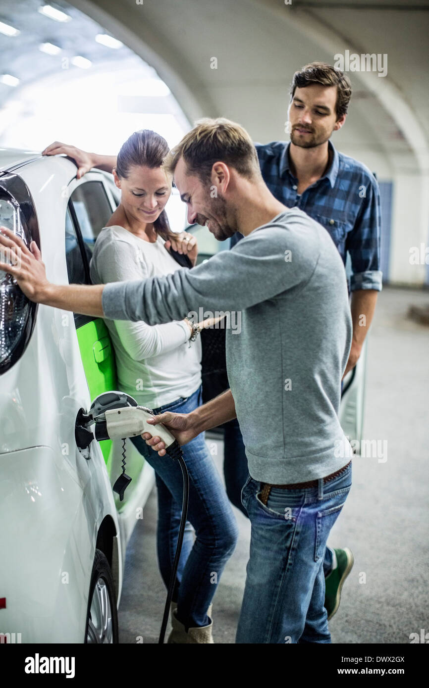 Freunde Blick auf Menschen, die Elektro-Auto in Tankstelle aufladen Stockfoto