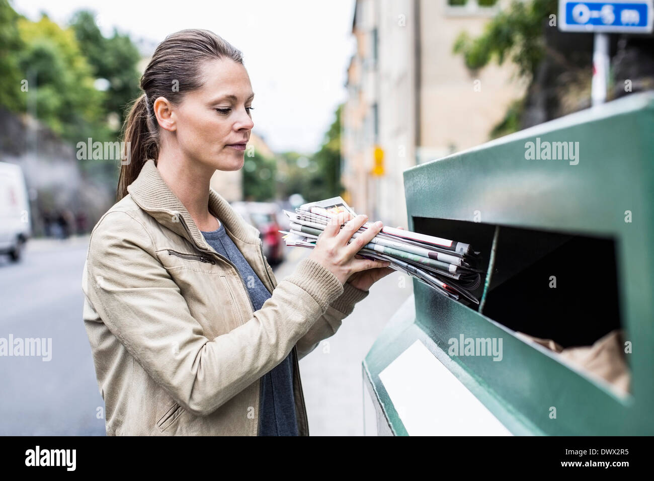 Mitte Erwachsene Frau Inbetriebnahme Zeitungen Recyclingbehälter Stockfoto