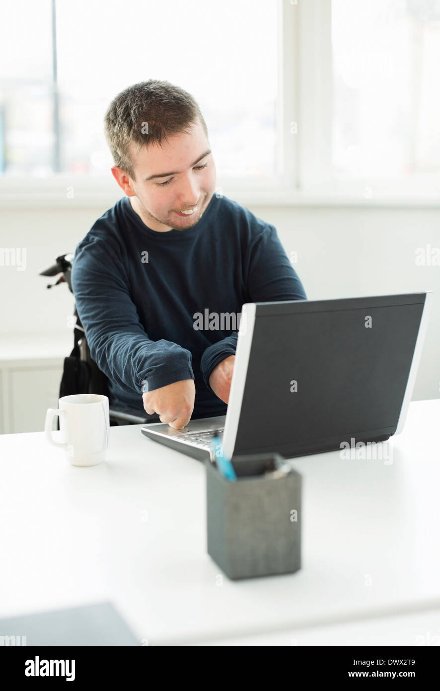 Junger Geschäftsmann mit zerebraler Lähmung mit Laptop im Büro Stockfoto