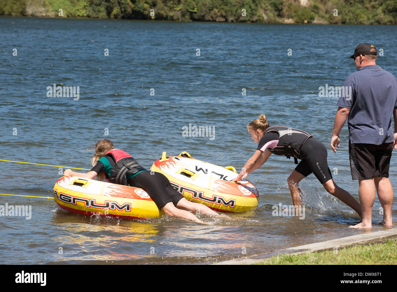 Zwei Mädchen im Teenageralter fahren aufblasbaren Donut, gezogen von einem Schnellboot an einem Fluss in der Moana Roa Reserve North Island NZ Stockfoto
