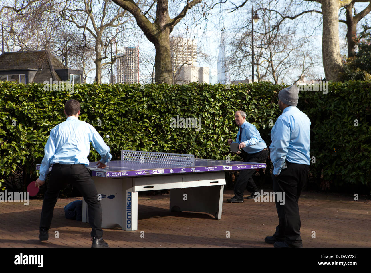 3 Männer in blauen Hemden Tischtennis in Victoria Embankment Gardens, London Stockfoto