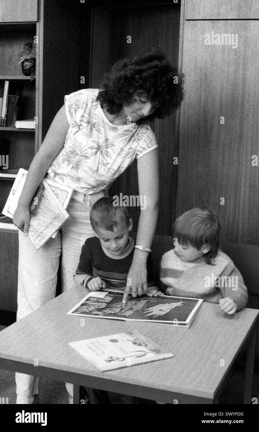 Berlin, DDR, Kinder im Vorschulalter Aussehen mit einem Bibliothekar ein Buch auf Stockfoto
