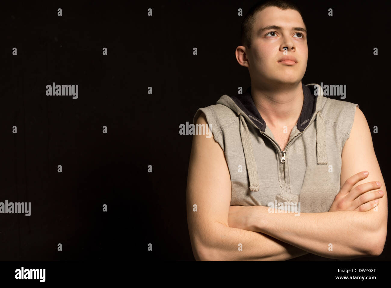 Hübscher junger Mann verlor in Kontemplation stehend mit seiner Arme gefaltet nach oben in die Luft mit einem schweren nachdenklichen Ausdruck, dunklen Hintergrund mit Exemplar. Stockfoto