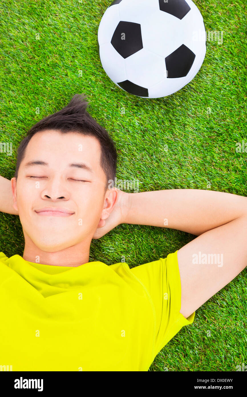 junger Mann mit einem Fußball auf einer Wiese liegend Stockfoto