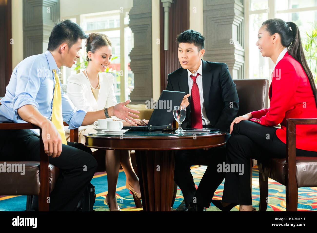 Vier asiatische chinesische Büro oder Unternehmer und Unternehmerinnen, die ein Geschäftstreffen in einer Hotellobby Dokument diskutieren Stockfoto
