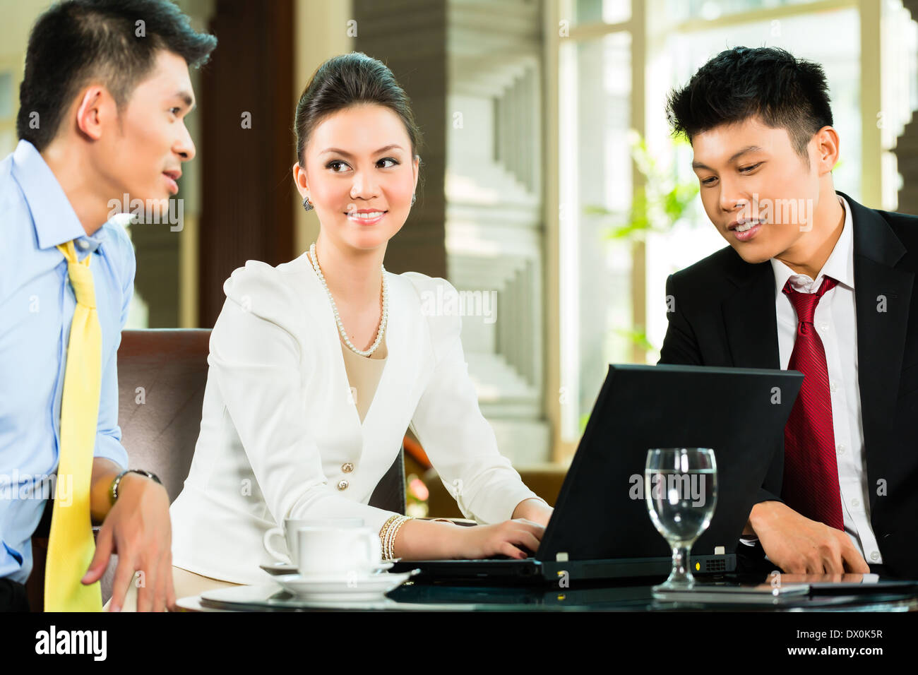 Drei asiatische chinesische Büro Menschen oder Geschäftsleute und Geschäftsfrau, die ein Geschäftstreffen in einer Hotellobby Dokument diskutieren Stockfoto