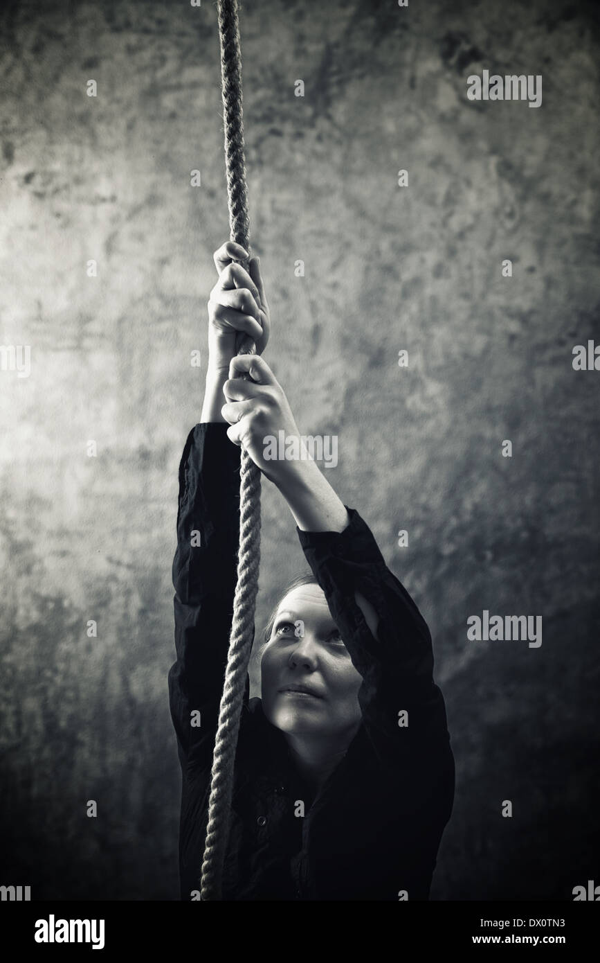 Frau mit Seil klettern. Überwindung der Probleme, Hindernisse und Schwierigkeiten im Leben Metapher. Stockfoto