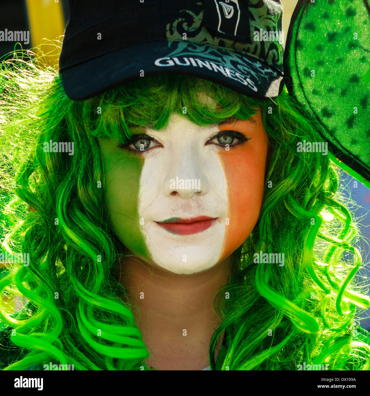 Junge Frau mit ihrem Gesicht in den Farben der irischen Flagge während der Feierlichkeiten zum St. Patrick's Day. Stockfoto