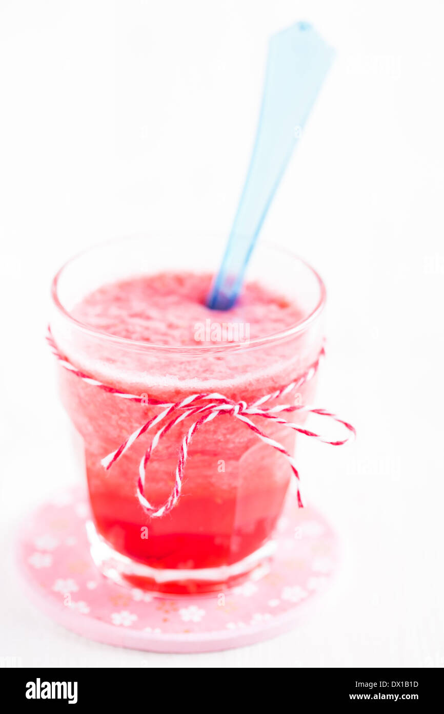 Nahaufnahme von Erdbeer Smoothie und blauen Plastiklöffel in Glas auf rosa Teller Stockfoto