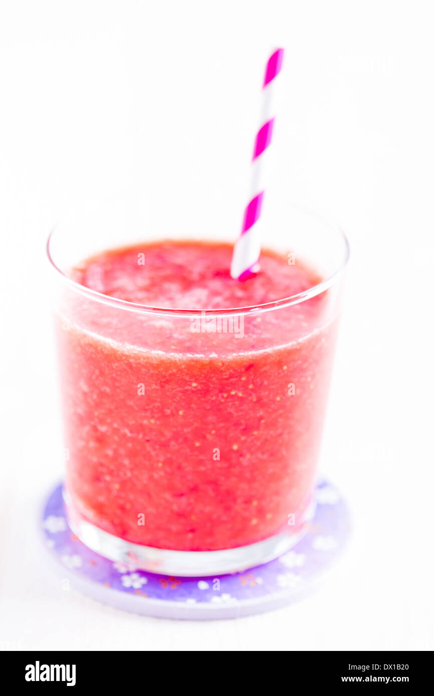 Nahaufnahme von Erdbeer Smoothie und gestreiften Stroh in Glas auf lila Teller Stockfoto
