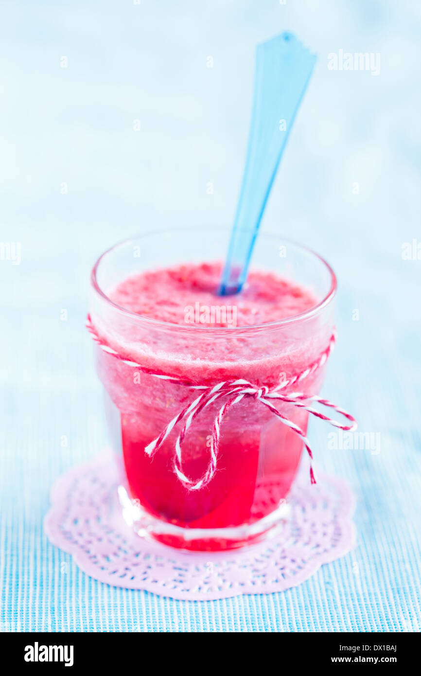 Nahaufnahme von Erdbeer Smoothie und blauen Plastiklöffel in Glas auf rosa Mat ruht auf leichte blaue Tischdecke Stockfoto