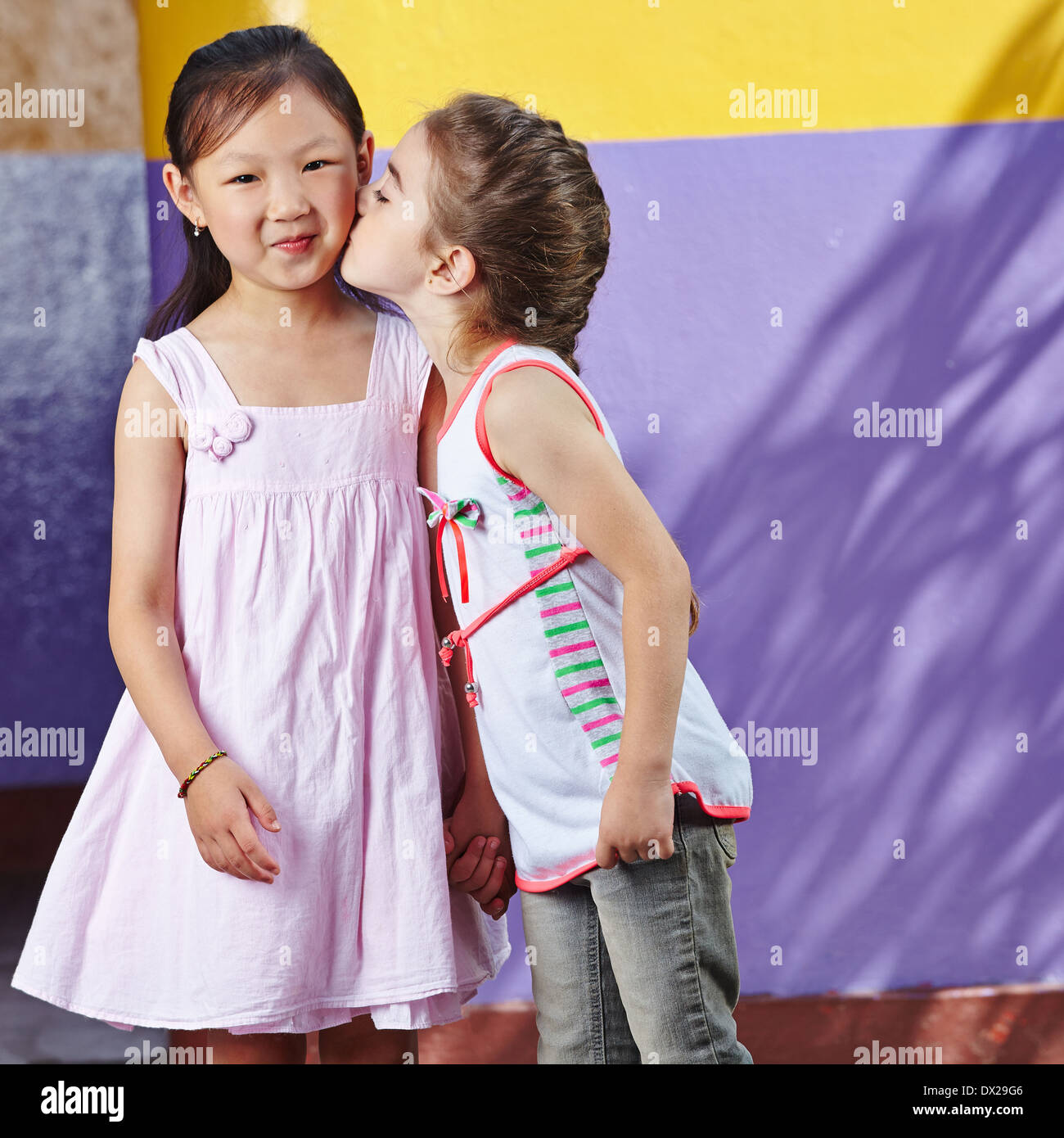 Mädchen küssen Freundin lächelnd während des Spielens im kindergarten Stockfoto