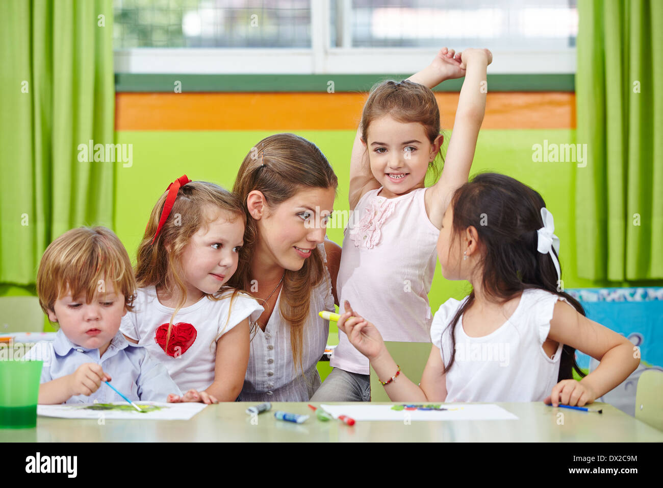 Kinder im Gespräch mit Kindergärtnerin im Kindergarten beim Bilder malen Stockfoto