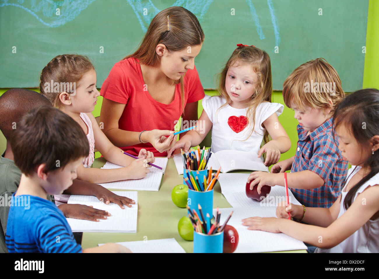 Kinder lernen gemeinsam in der Vorschule mit Kindergärtnerin schreiben Stockfoto
