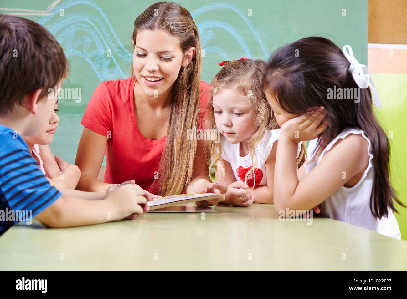 Viele Kinder am Tisch ein Buch mit Kindergärtnerin in der Vorschule Stockfoto