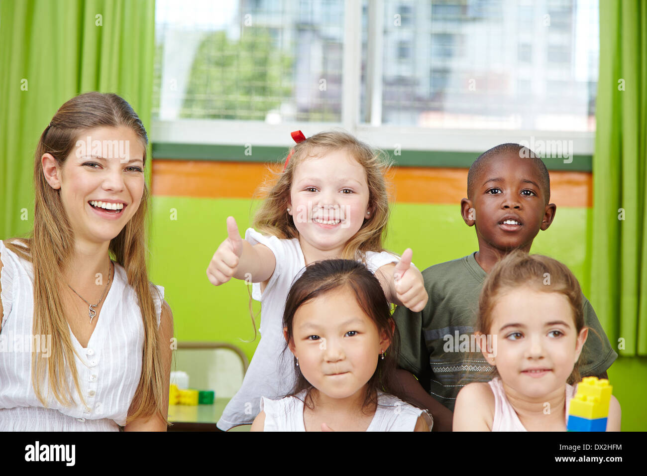 Glückliches Mädchen im Kindergartengruppe mit Lehrer ihre Daumen hochhalten Stockfoto