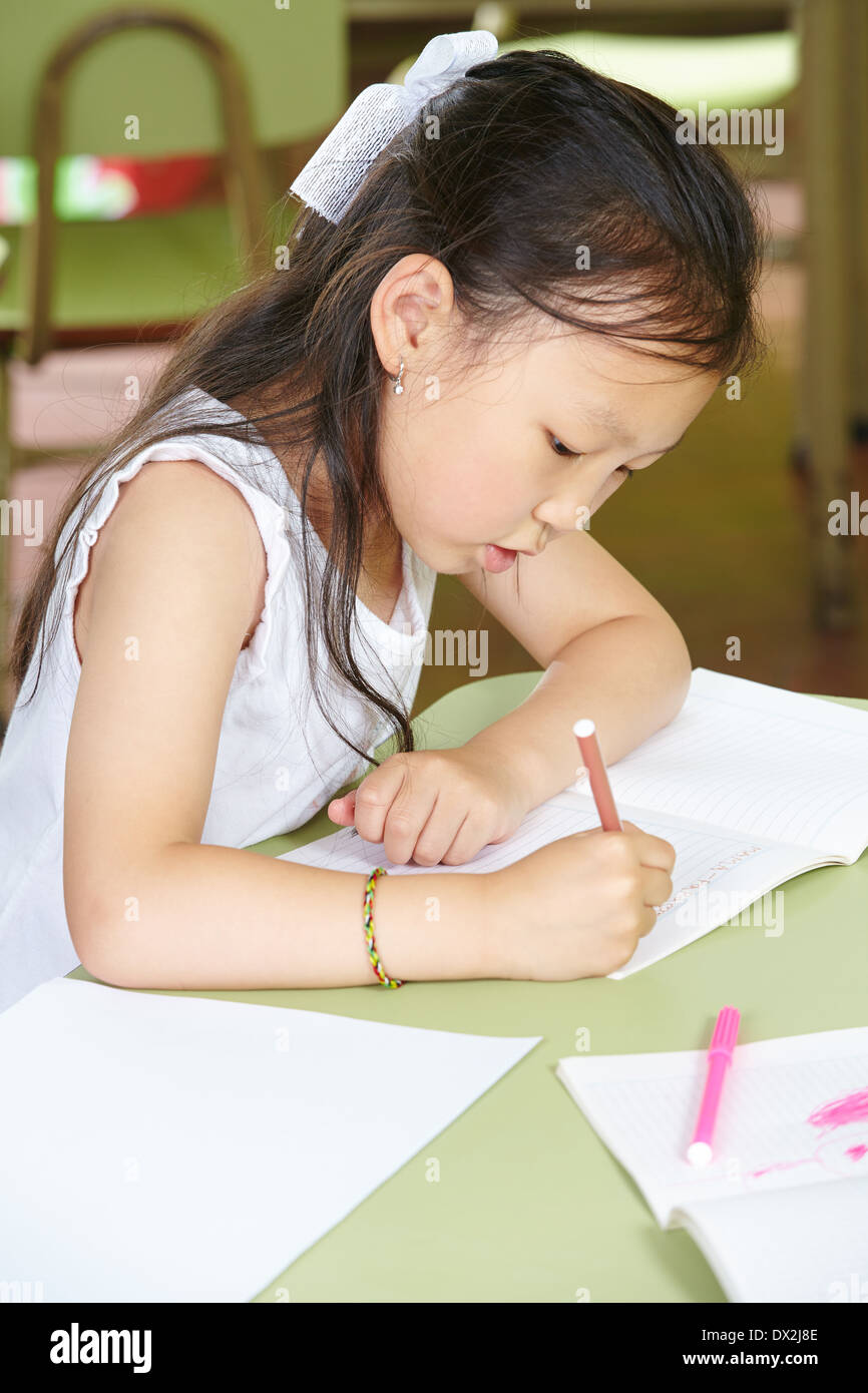 Chinesisches Mädchen lernen im Kindergarten mit einem Stift an einem Tisch zu schreiben Stockfoto