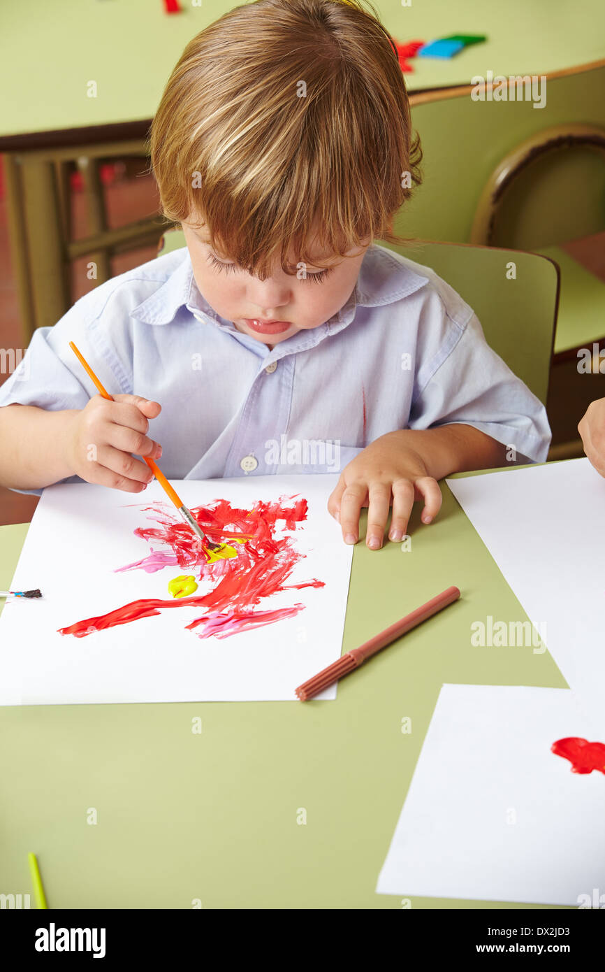 Jungen im Kindergarten mit Pinsel und Farbe auf Papier zeichnen Stockfoto