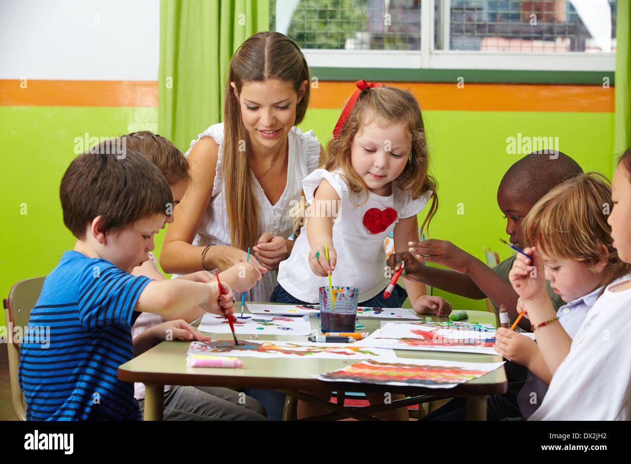Viele Kinder malen gemeinsam mit Kindergärtnerin in einem kindergarten Stockfoto